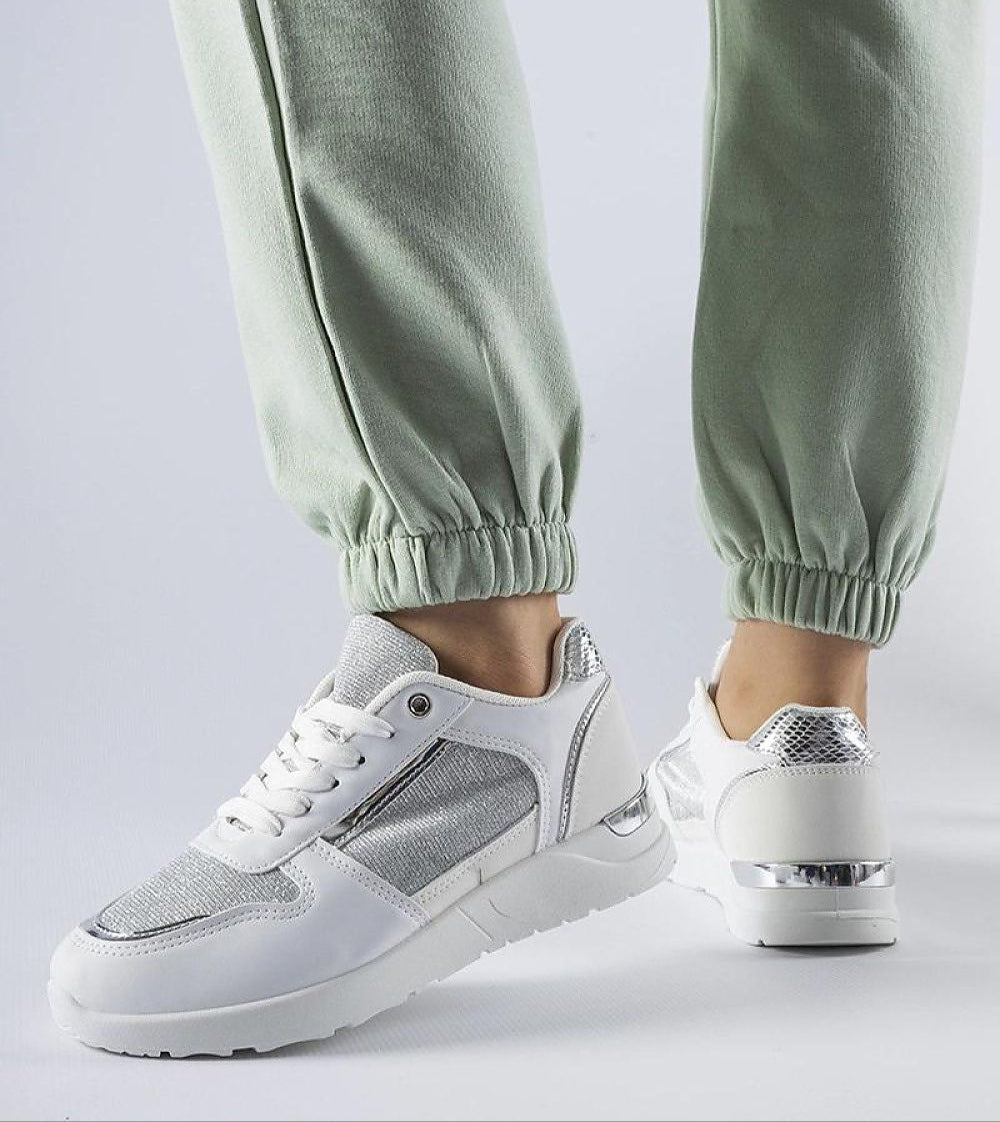 Woman wearing green pants and Facondo white lace-up sneakers with decorative stitching and white rubber sole, side view.
