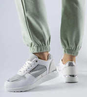 Woman wearing green pants and Facondo white lace-up sneakers with decorative stitching and white rubber sole, side view.
