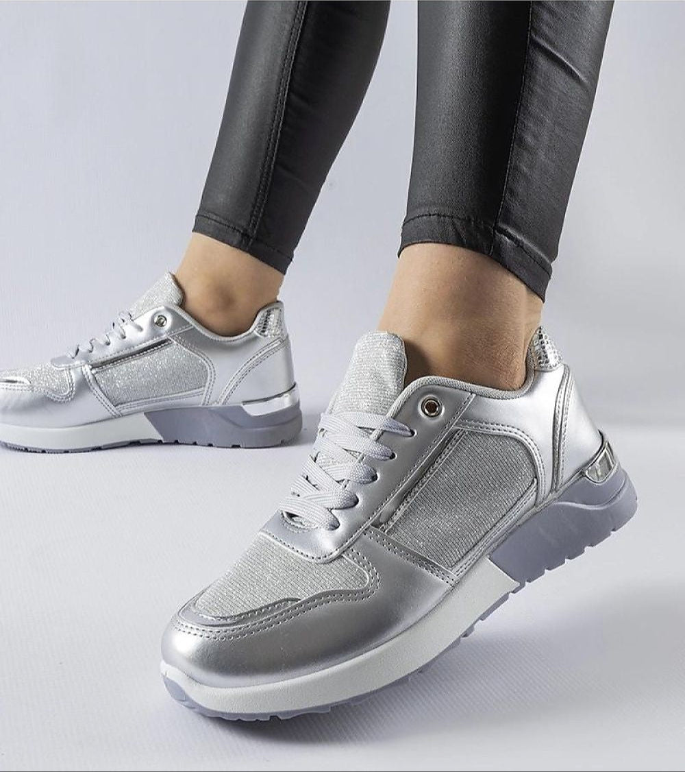 Silver lace-up sneakers worn with black leggings on a white background.