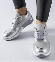 Silver metallic lace-up sneakers paired with black leggings on white background.