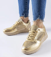 Gold metallic sneakers with lace-up design, worn with frayed-edge blue jeans, highlighting contemporary style and casual elegance.