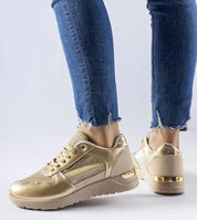 Person wearing gold sneakers with denim jeans, showing side view of stylish footwear.