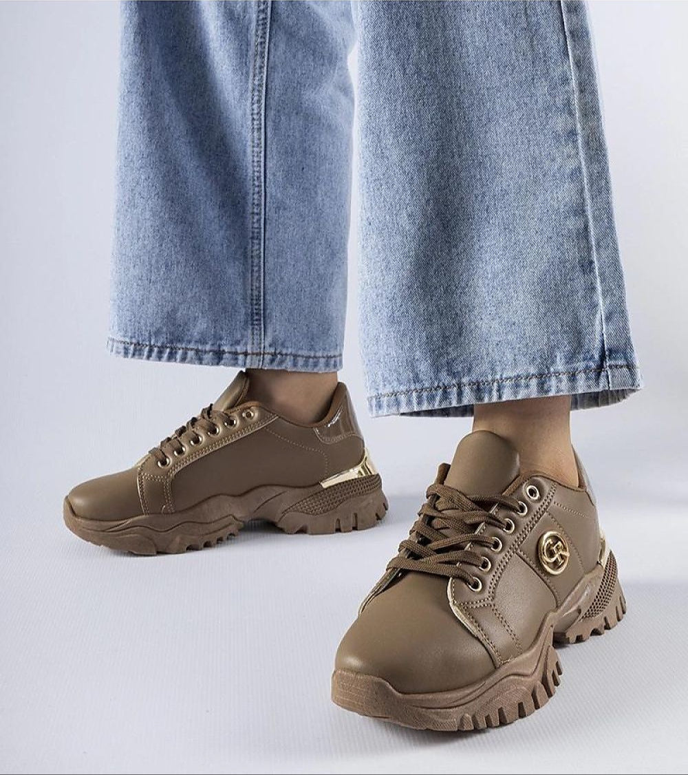 Woman wearing Arpaia Chunky Brown Sneakers with denim jeans, featuring a bold design, eco leather, and a thick rubber sole.