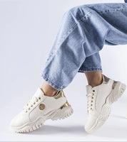 Person wearing cream sneakers with chunky sole and gold accents with light blue jeans.