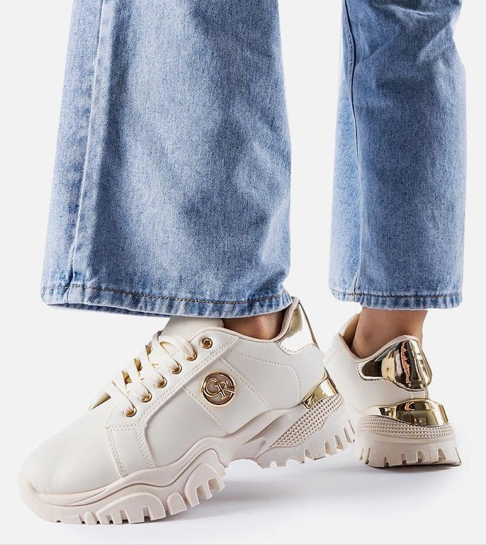 Person wearing chunky white sneakers with gold accents and blue jeans.