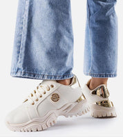 Person wearing chunky white sneakers with gold accents and blue jeans.
