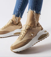 Fashionable brown and white sneakers with decorative stitching, worn with distressed jeans, showcasing eco-leather and stable rubber soles.
