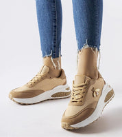 Woman wearing tan and white sneakers with embellishments, paired with distressed jeans, showing side view of stylish footwear.