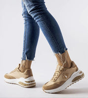 Person wearing stylish tan sneakers with white soles and gold bee embroidery, paired with ripped blue jeans.