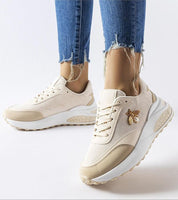 Beige sneakers with gold bee detail and white sole, worn with distressed jeans.