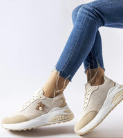 Beige modern sneakers with gold accents worn with frayed hem blue jeans, showcasing stylish and comfortable footwear.