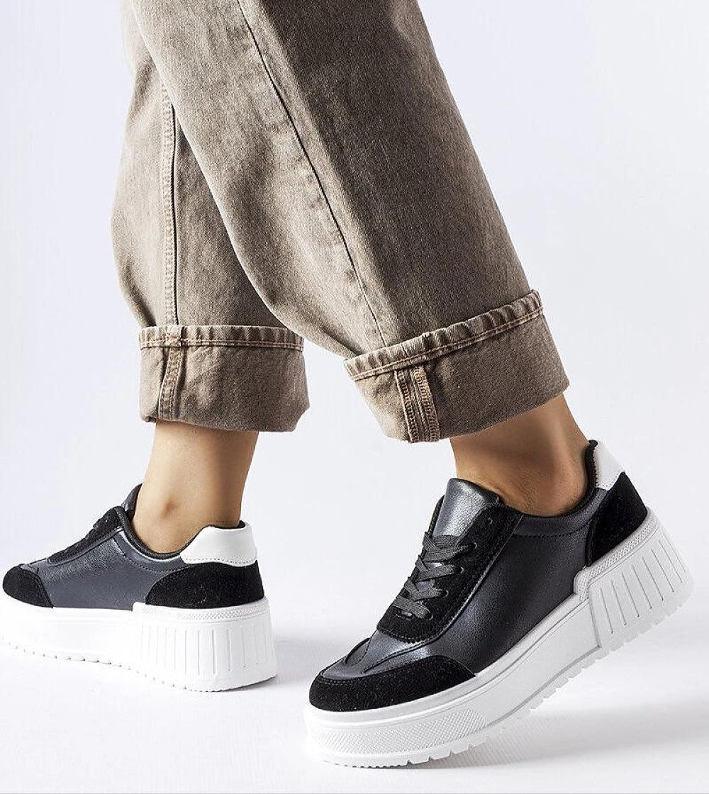 Person wearing dark sneakers with a thick white sole and black lace-up, styled with cuffed beige pants for a casual look.