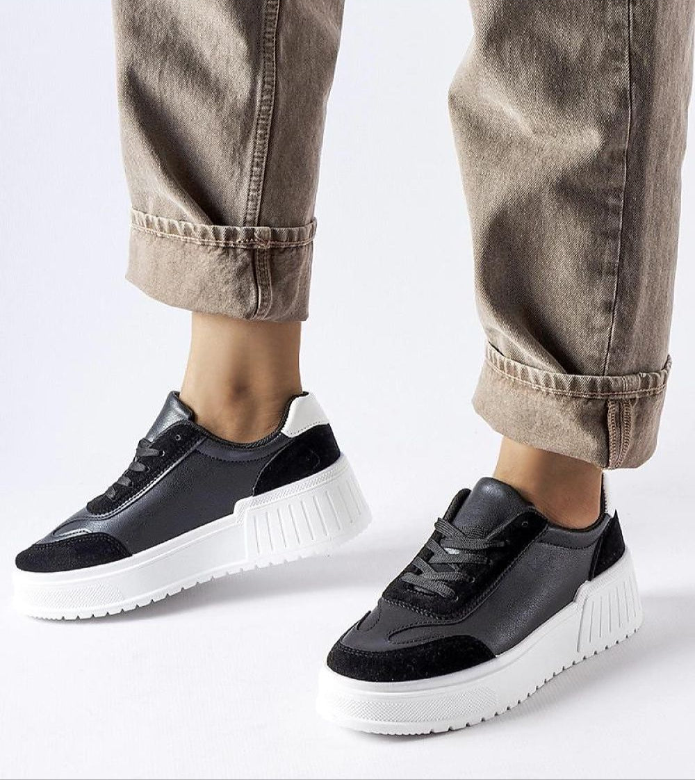 Person wearing stylish black and white platform sneakers with rolled-up beige pants, showcasing casual street fashion.