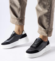 Person wearing stylish black and white platform sneakers with rolled-up beige pants, showcasing casual street fashion.