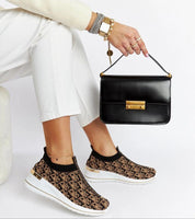Woman wearing Marronza Slip-On Wedge Sneakers with a black handbag, showcasing the stylish black-brown textile and medium wedge design.