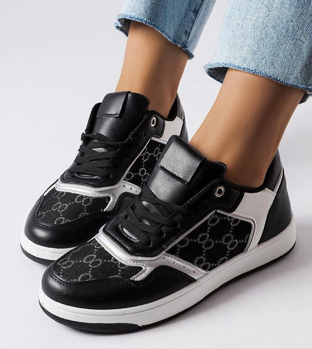 Black and white sneakers with monogram pattern and lace-up design, shown on feet wearing denim jeans.