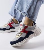 Person wearing gray sporty lace-up sneakers with red and navy accents, featuring a thick white sole, paired with blue jeans.