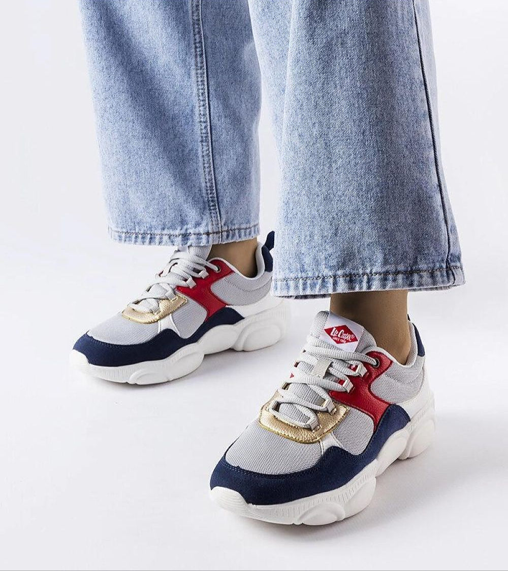 Person wearing trendy lace-up sneakers with blue, red, and white accents, paired with denim jeans, studio background.
