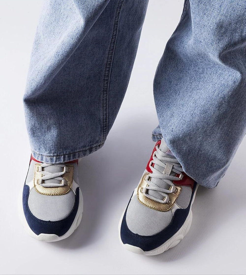 Person wearing gray lace-up sneakers with gold accents and denim jeans, showing sporty and comfortable design for active days.