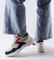 Person wearing sporty sneakers with navy and red detailing, white sole, and casual jeans, showcasing urban style.