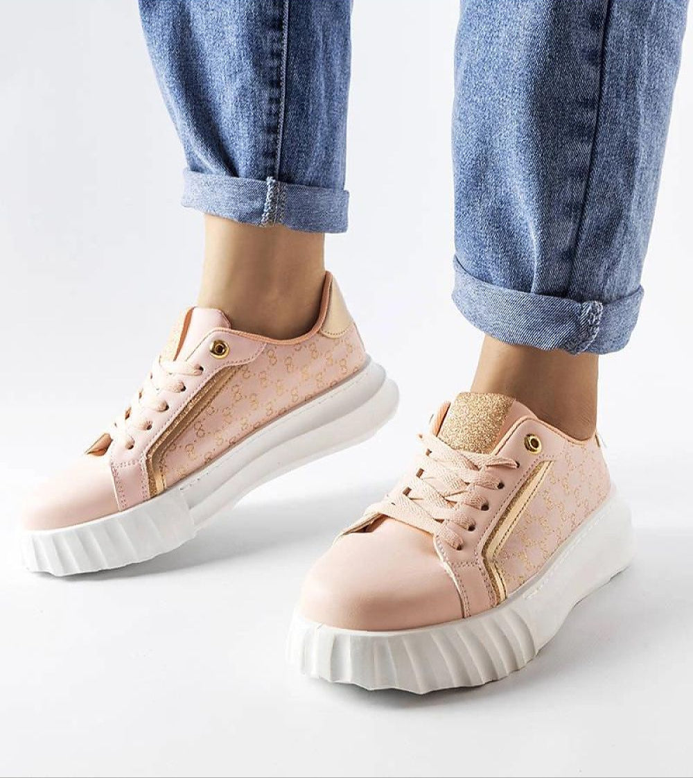Person wearing pink platform sneakers with gold accents and white sole, paired with rolled-up jeans against a white background.