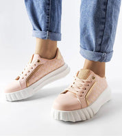 Person wearing pink platform sneakers with gold accents and white sole, paired with rolled-up jeans against a white background.