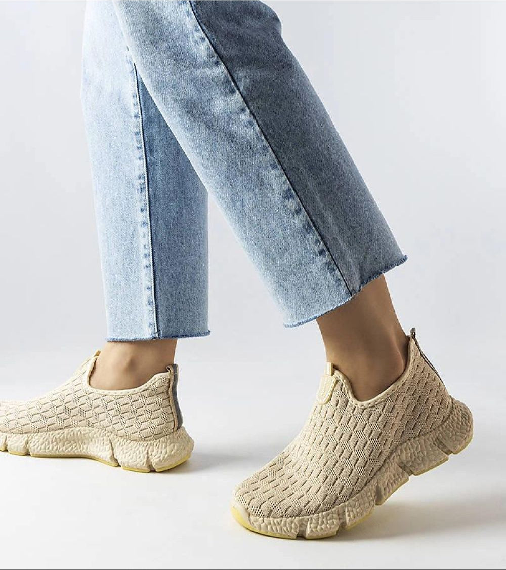 Person wearing Orellia Light Beige Slip-On Sneakers with blue jeans, showcasing breathable fabric and beige cushioned sole.