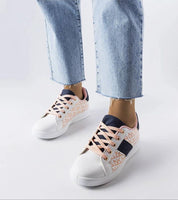 Model wearing Alelya Doringer StrideGlow Sneakers with pink laces and color accents, paired with rolled-up denim jeans.