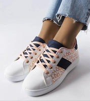 Woman wearing Alelya Doringer StrideGlow Sneakers with white eco-leather and colorful designs, paired with blue jeans.