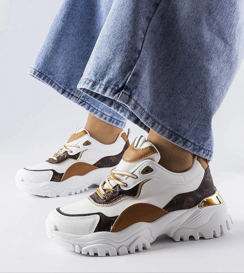 Stylish white and brown sneakers with irregular sole and gold detailing worn with blue jeans.