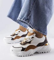 Stylish white and brown sneakers with irregular sole and gold detailing worn with blue jeans.