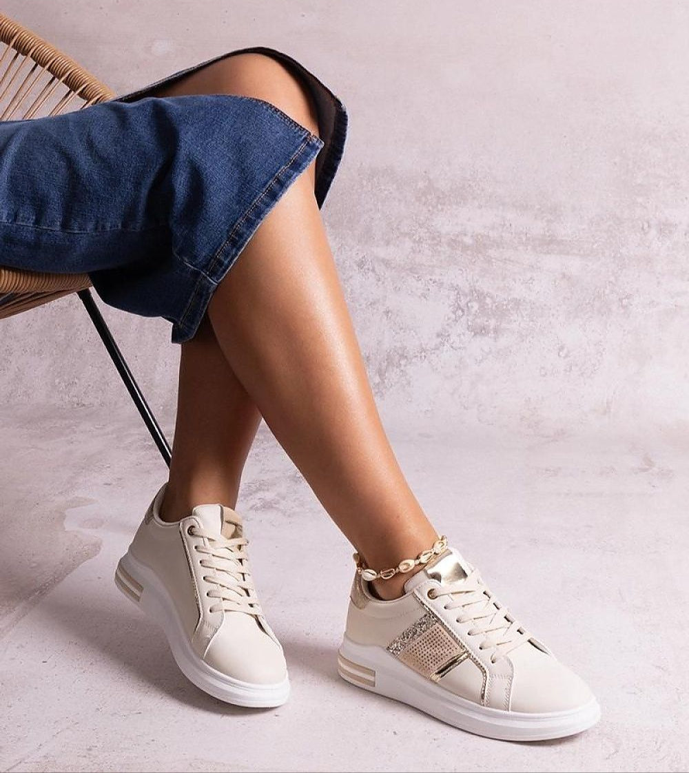 Woman wearing Meralla Rhinestone Platform Sneakers, featuring beige tone and shimmering rhinestone details, sitting casually with denim jeans.