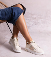 Woman wearing Meralla Rhinestone Platform Sneakers, featuring beige tone and shimmering rhinestone details, sitting casually with denim jeans.