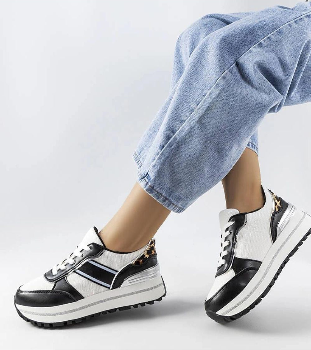 Fashionable black and white sneakers with animal print accents paired with rolled-up denim jeans, showcasing a modern casual style.
