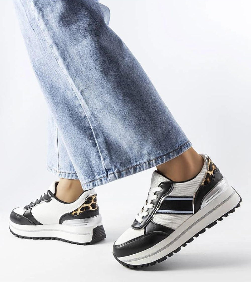 Black and white platform sneakers with lace-up closure, featuring leopard print details on heel, paired with light blue jeans.