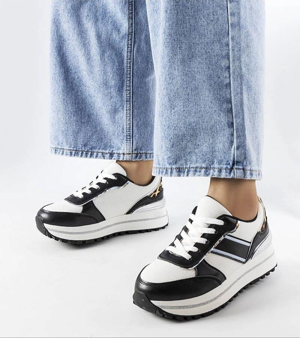 Fashion sneakers with black and white design, worn by a person in blue jeans, featuring a trendy and comfortable look.