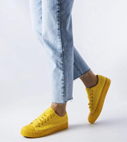 Bright yellow woven sneakers with lace-up closure, worn with light jeans, highlighting casual summer style.