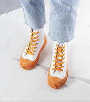 Person wearing Ossavine Fabric Platform Lace Sneakers in white with orange soles and laces on a marble floor.