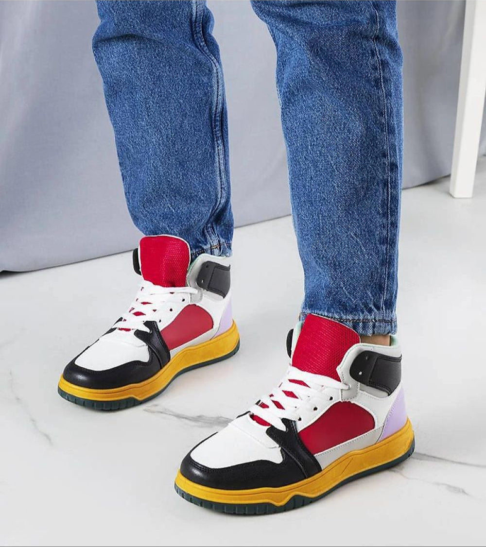 Colorful high-top sneakers with red, black, and white design, featuring yellow soles, worn with blue jeans on a marble floor.