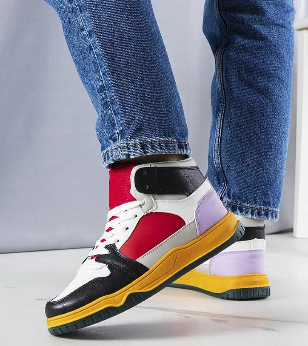 Colorful high-top sneakers with red, black, and purple panels worn by a person in blue jeans, showcasing street style fashion.