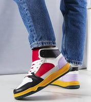 Colorful high-top sneakers with red, black, and purple panels worn by a person in blue jeans, showcasing street style fashion.
