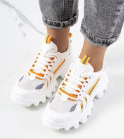 Person wearing white and orange platform sneakers with reflective trim and sculpted rubber sole on a marble floor.