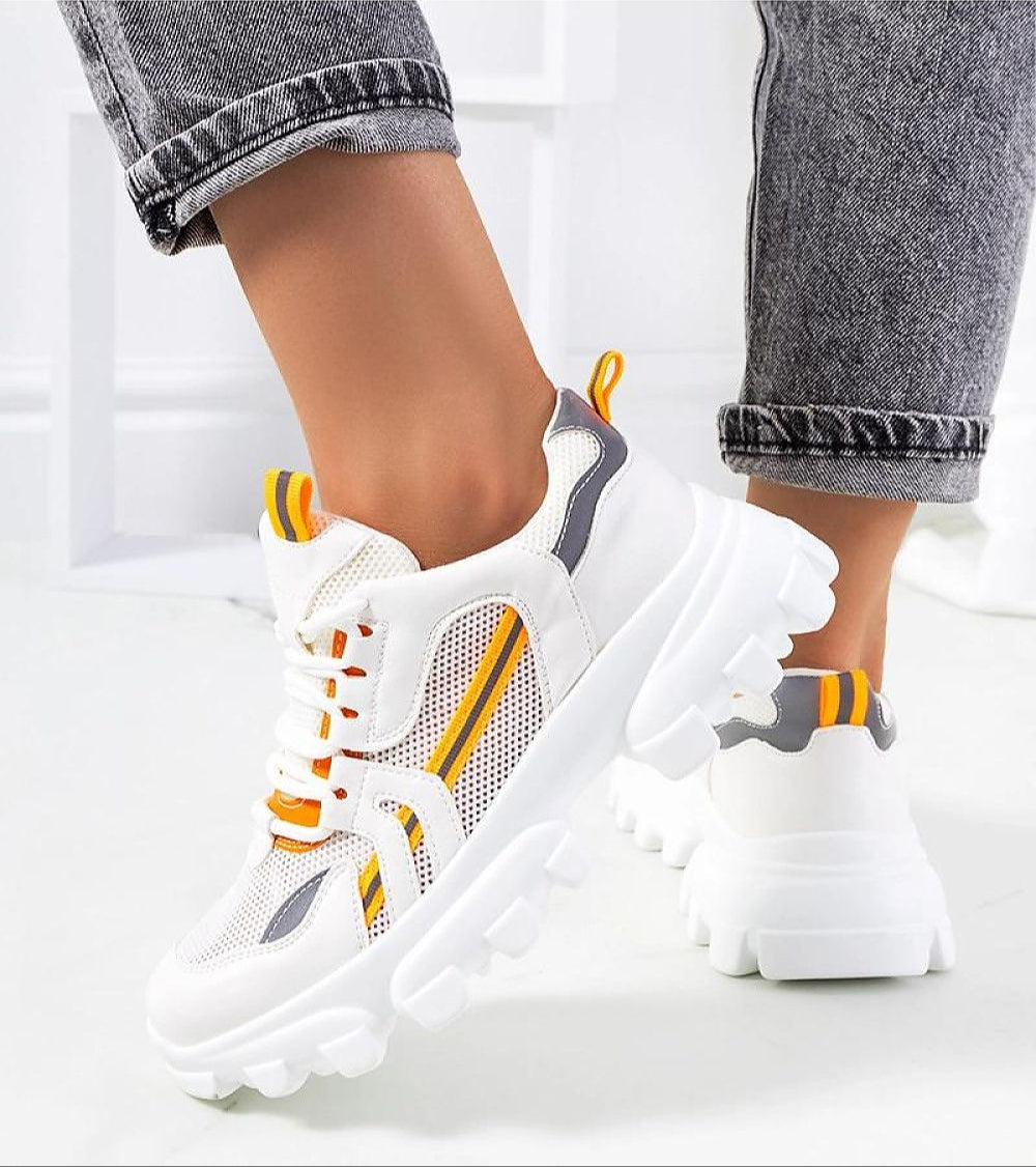 Sporty white platform sneakers with reflective trim and orange accents worn with jeans.