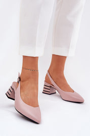 Woman wearing Elorelle Column-Heel Sandals in pink eco leather with ankle strap and pointed toe, paired with white trousers, day or evening wear.