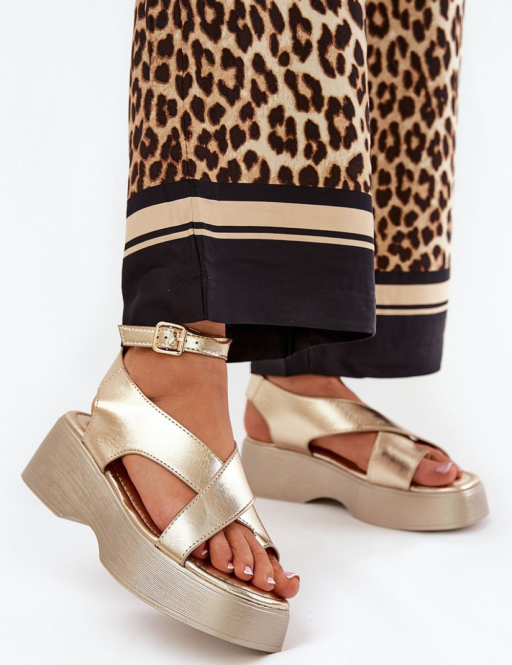 Gold Lirianne Platform Buckle Sandals with wedge heel, open toe, and ankle strap, paired with leopard print pants, for stylish ease.