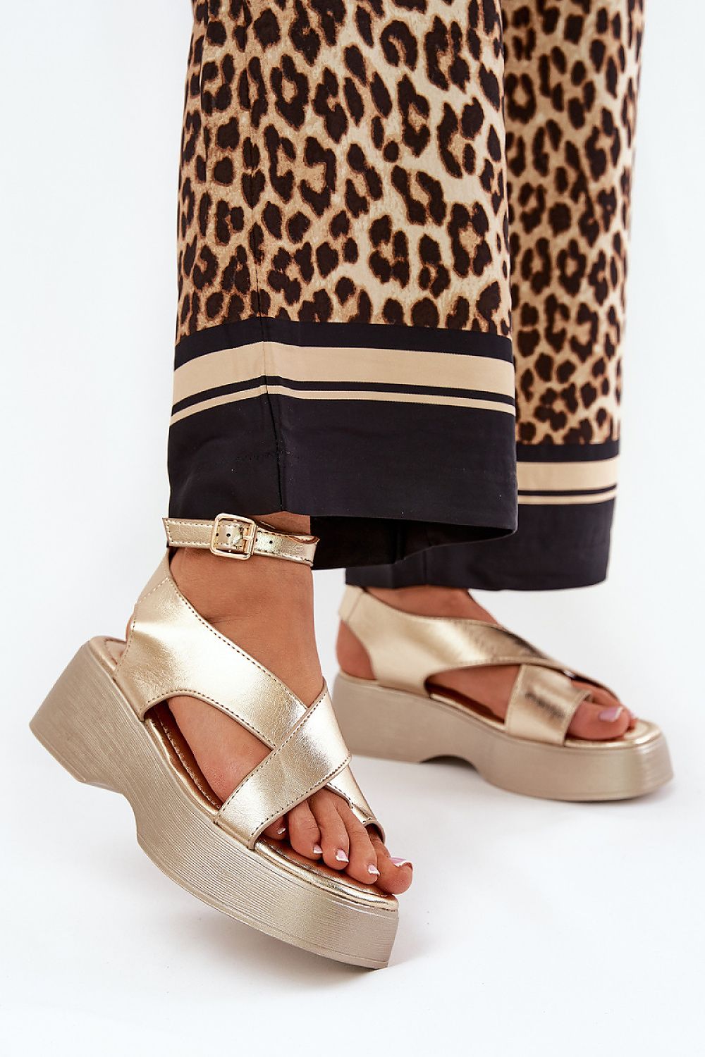 Gold Lirianne Platform Buckle Sandals with wedge heel, open toe, and ankle strap, paired with leopard print pants, for stylish ease.