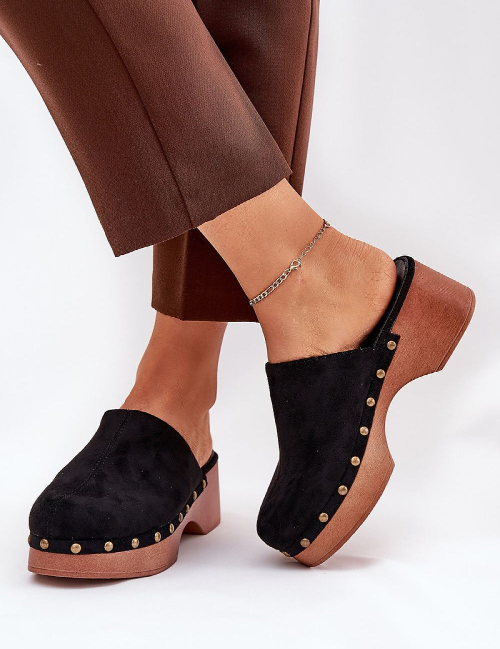 Black studded suede wedge clogs with bohemian charm, featuring eco suede and cushioned insoles, paired with brown trousers.
