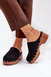 Black studded suede wedge clogs with bohemian charm, featuring eco suede and cushioned insoles, paired with brown trousers.