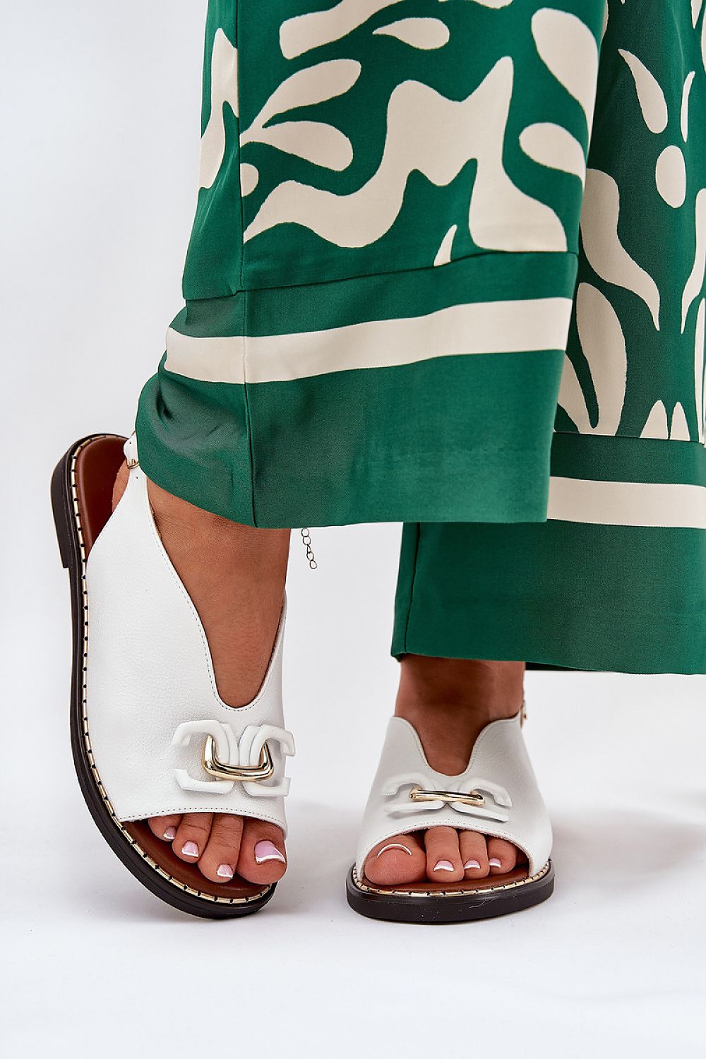 Almira flat eco-leather sandals with decorative front detail and adjustable buckle, paired with green patterned trousers.