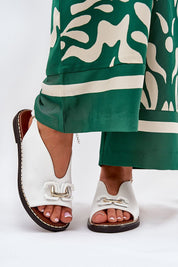 Almira flat eco-leather sandals with decorative front detail and adjustable buckle, paired with green patterned trousers.